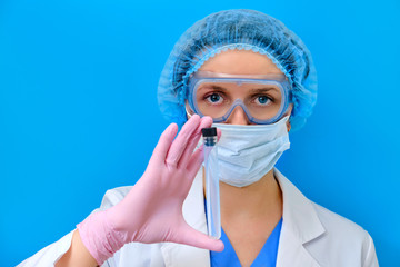 A doctor in protective medical clothing from viruses holds a test tube for analysis, blue background. Nurse in a medical mask with a flask for microbiological research
