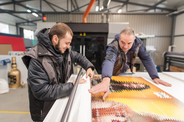 Two technicians glue poster to foam. Semi automatic gluing machine