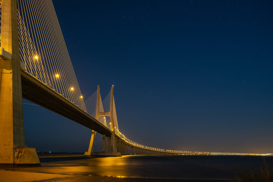 Illuminated Suspension Bridge Over River At Night