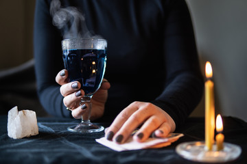 Female hands holding magic love potion and occultic fortune-telling cards on dark background