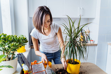 Beautiful smiling girl with braces replanting a indoor flower. Wearing a white T-shirt and blue...
