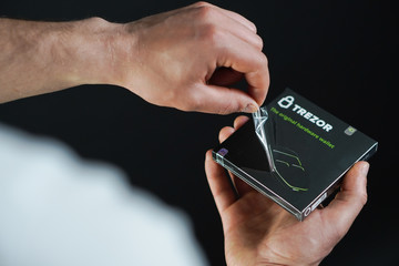 Detail of man's hand unboxing the crypto hardware wallet - Trezor on the black background. 