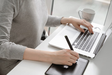 A young woman is working on a laptop at home near the window