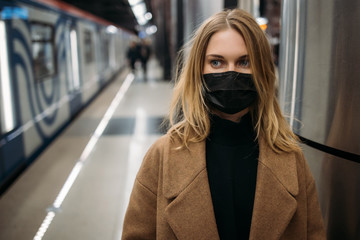 Fototapeta premium Blonde woman in black medical mask, in coat standing in subway.