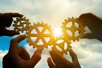 Four hands of businessmen assemble gears into a puzzle in a single whole against the backdrop of...