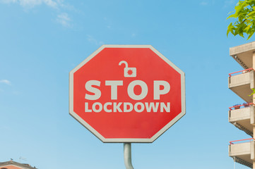 Stop lockdown concept: a stop street sign with the text stop lockdown with a blue sky on the background and some houses and trees around