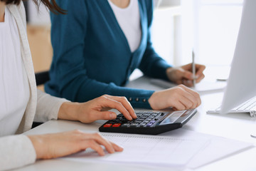 Accountant checking financial statement or counting by calculator income for tax form, hands closeup. Business woman sitting and working with colleague at the desk in office toned in blue. Tax and