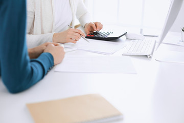 Accountant checking financial statement or counting by calculator income for tax form, hands closeup. Business woman sitting and working with colleague at the desk in office toned in blue. Tax and