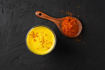 Saffron latte in a glass cup on a black concrete background, wooden spoon with spice saffron,golden...