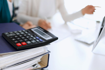 Calculator and binders with papers are waiting to be processed by business woman or bookkeeper working at the desk in office back in blur. Internal Tax and Audit concept