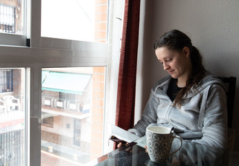 Fototapeta na wymiar Girl reading a book by the window while having a tea