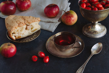 Tea with rosehip berries in a vintage cup with apple charlotte and apples on a dark background