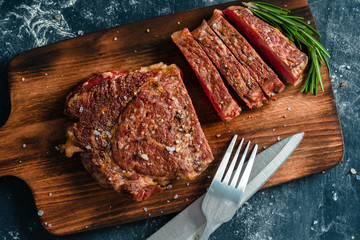 Beef steak with coarse salt and a sprig of rosemary on a wooden cutting board against a dark background