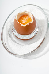 Soft-boiled egg on a glass stand with coarse salt on a white background