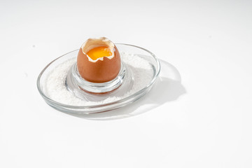 Soft-boiled egg on a glass stand with coarse salt on a white background