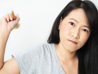 Asian woman wearing a gray T-shirt was angry and upset until she threw makeup brush to camera. Lady has dark brown long hair. Female makeup pink nude tone color. White backdrop isolated background.