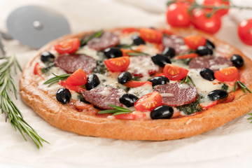 Pizza with sausage and cherry tomatoes on a sheet of baking paper