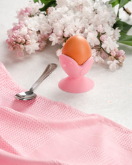 Soft-boiled egg on a pink stand with a spoon and lilac flowers on a light background