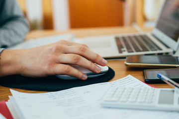 hand moving the computer mouse. Girl working at home with her laptop, calculator and mobile phone