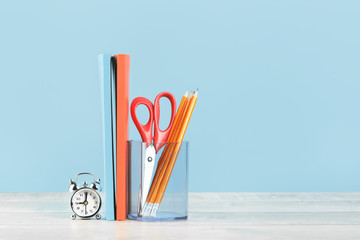 Organized office and school orange and pastel blue stationery, notebooks pencils scissors and alarm clock on grey wooden desk. Copy space for back to school or education knowledge and craft concept