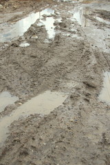 Dirty dirt road with track, wheel marks, brown clay and puddles in Russia.