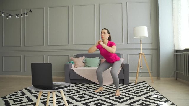 Young Woman Doing Exercises While Watching Training Online Session on a Laptop in the Living Room. Lifestyle and Healthy Body Concept