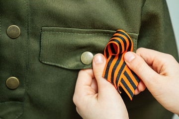 St. George's ribbon is fixed by the hands of a girl on the military uniform. Concept of memory,...