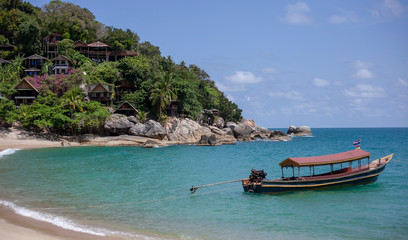 Fototapeta na wymiar Small houses on the mountain in the jungle and a boat on the beach in Thailand on the island of Phangan. Natural background with blue sea.