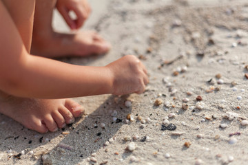 A small child plays in the sand on the beach. Only arms and legs are visible.