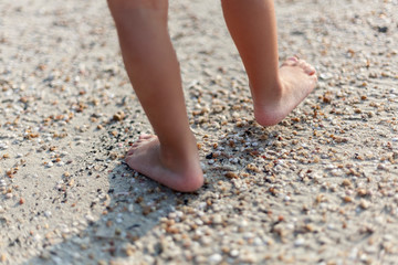 Little feet of a child walk on a sandy beach in the evening.