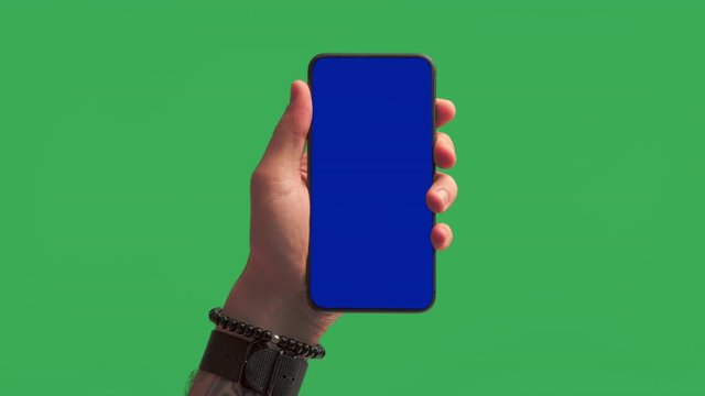 High quality mock up template of millennial hipster man hand reveal smartphone with blue chroma key screen on green background