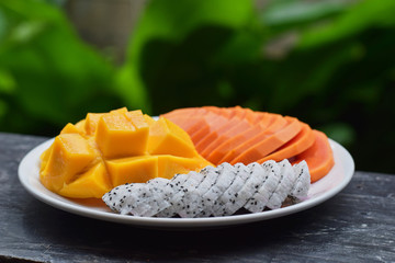 Plate with tropical fruits. Papaya, mango, dragon fruit on a plate on a green background. Thai fruits.