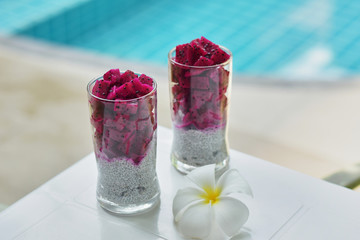 Two glasses with chia seed pudding and fruit dragon near the pool. Chia pudding  on the background of the pool. Thai fruits.