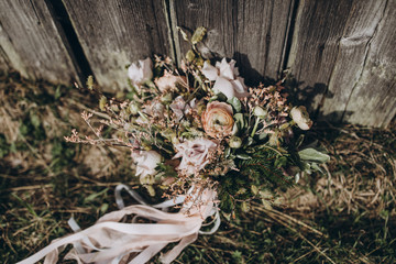 Floristics Bridal bouquet. A bouquet of flowers and greenery with pink ribbons stands on the grass near the wooden wall of the old barn.