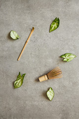 Matcha tea accessories and leaves on a gray surface.