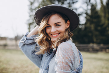 Portrait of the bride. Country style. A young girl in a blue gray wedding dress, denim jacket and hat with a bouquet of flowers and greenery in her hands on a background of a forest and a wooden fence