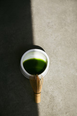 Chawan bowl with matcha tea and a bamboo whisk divided by shadow on a gray background.