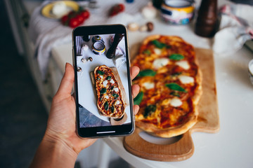 Selective focus on smartphone, person makes photo of fresh baked homemade pizza at home. Learn new...