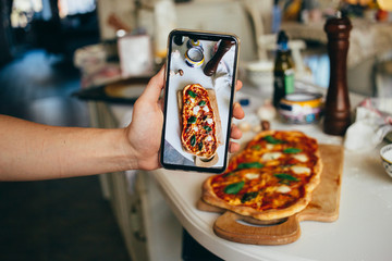 Selective focus on smartphone, person makes photo of fresh baked homemade pizza at home. Learn new...