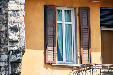 Fototapeta na wymiar Italian window on the yellow wall facade with open brown color classic shutters