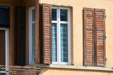 Italian windows on the yellow wall facade with open and closed brown color classic shutters
