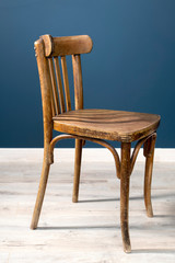 An old Viennese chair in a room against a dark blue wall and on a laminate