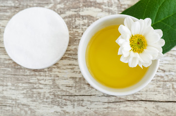 Small white bowl with cosmetic oil and cotton pad for natural skin care. Organic cleansing oil, make up remover. Top view, copy space.