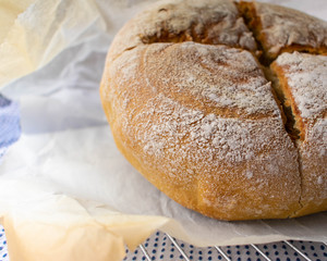An artisan style baked loaf of bread partially wrapped in parchment paper on a metal cooling rack.
