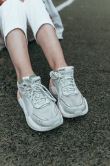 female legs in white sneakers on green grass. Football or soccer field. Sport shoes on textured surface. Copy space. Relax and rest time. Jogging concept. Tanned slim legs in white fitness footwear