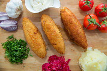 Ukrainian tradition food on a wooden board . Red cabbage sauerkraut in a small bowl . mashed potatoes . Mayonnaise, Garlic, Onion, Tomatoes. Chopped coriander.Chicken Kiev cutlets with parsley leaves.