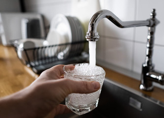 man filling a glass of water from a stainless steel kitchen tap. male's hand pouring water into the glass from chrome faucet to drink running water with air bubbles. potable water and safe to drink.