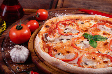 Appetizing pizza with peppers, mushrooms and ham on wooden background