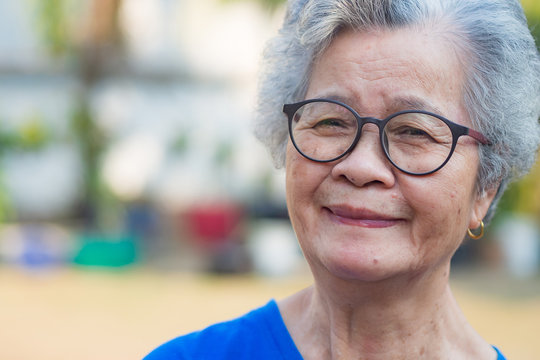 A portrait of an elderly woman short white hair wearing glasses smiling and looking at the camera while standing in a garden. Space for text. Concept of old people and health care