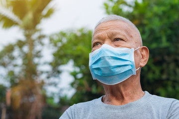 A portrait of an elderly man wearing a face mask looking up while standing in a garden. Mask for...